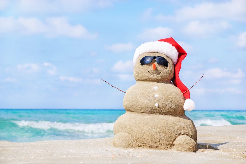 Smiling sandy snowman in red santa hat on the sea beach. Holiday concept can be used for New Year and Christmas Cards July