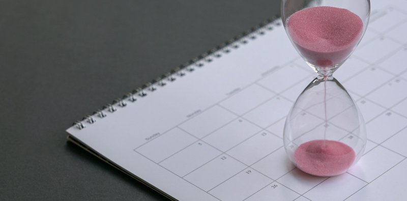 Hour glass with sand flowing,  sitting on calendar. Close up. Time management or deadlines concept.