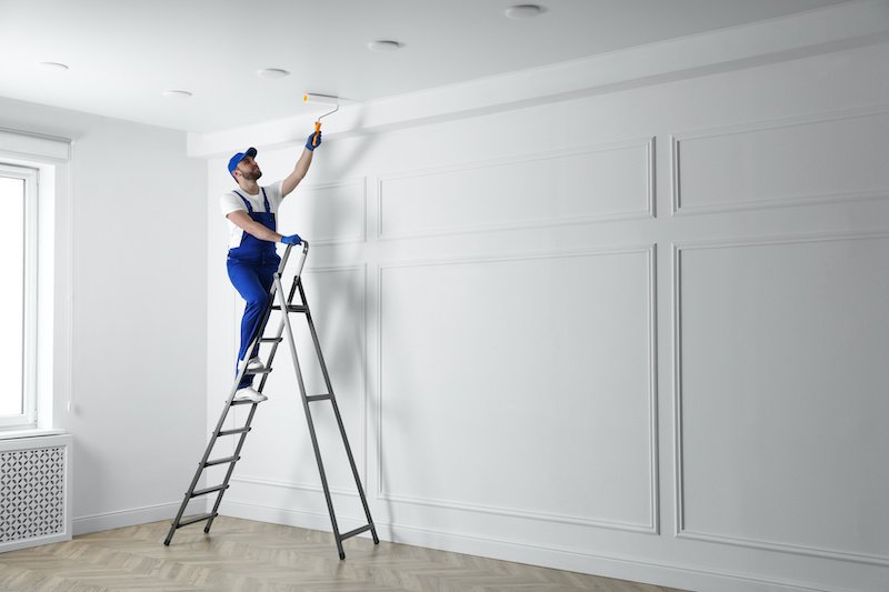 Handyman painting ceiling with white dye indoors, space for text ceiling painting