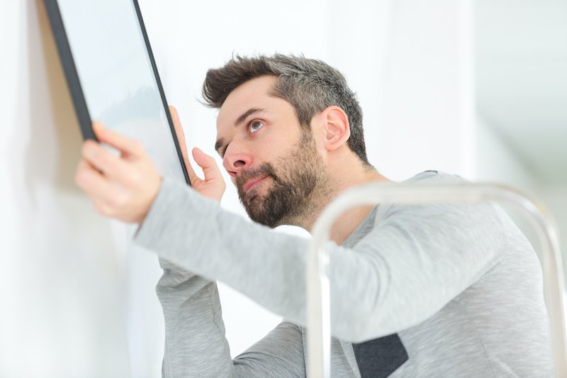 man hanging blank picture frame on wall