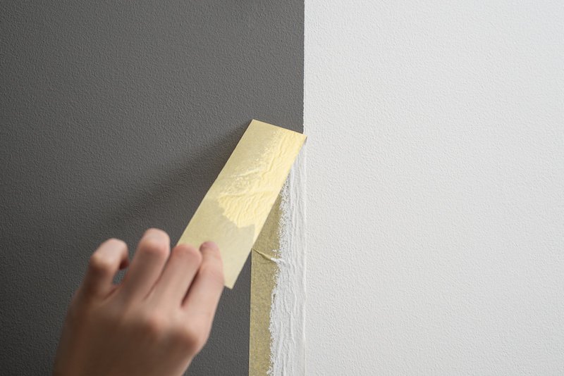 Hand taking off masking tape from the wall after painting. Home renovation tricks and minimalistic style.