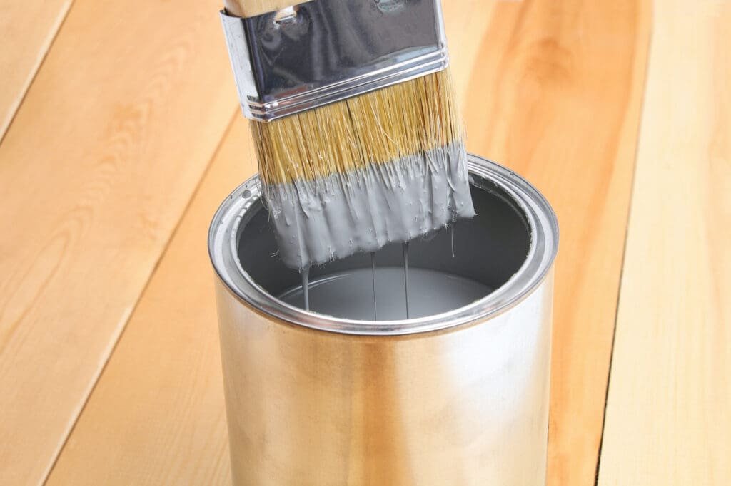 Brush with can paint in hand. A man paints wooden boards in a gray paint brush.