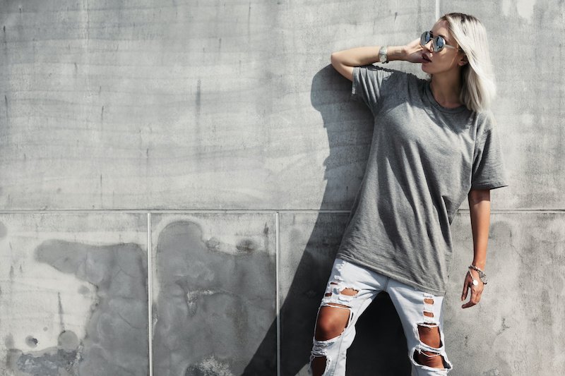 Hipster girl wearing blank t-shirt, fashion sunglasses and jeans posing against rough concgrete wall, minimalist street style