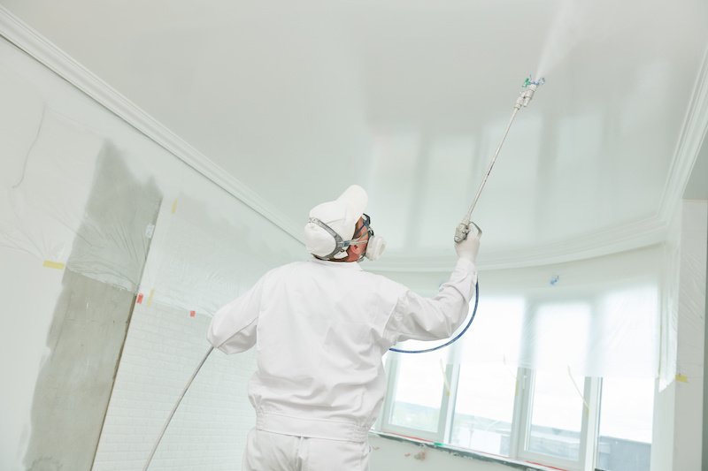Airless spray painting. Painter worker with sprayer jet painting ceiling surface into white color at home impovement and refurbishment