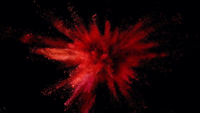 Explosion of coloured powder isolated on black background. Abstract colored background red color theory