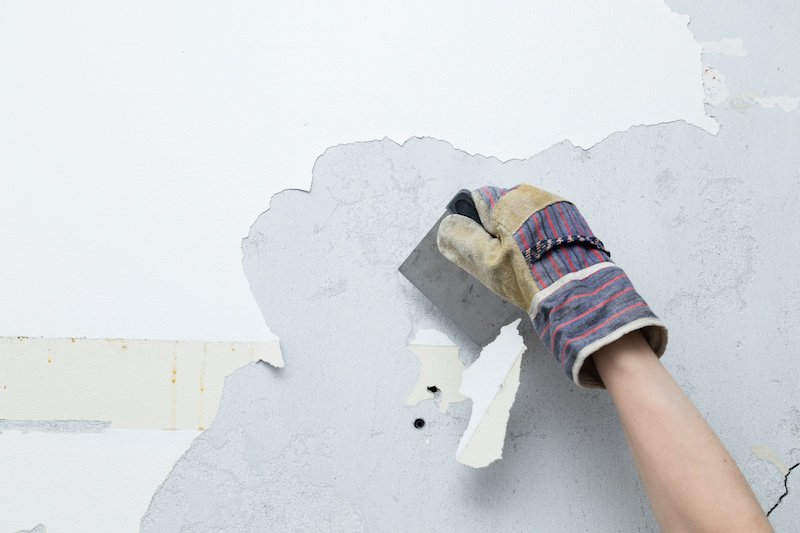 person scraping white paint of concrete wall during a home remodeling project