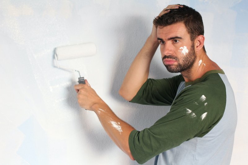 Exhausted man trying to paint a wall