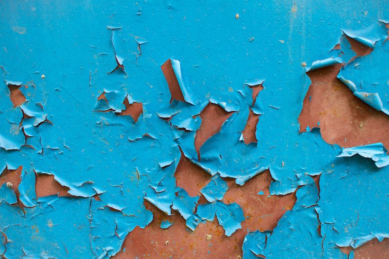Peeling blue paint on rusty metal wall