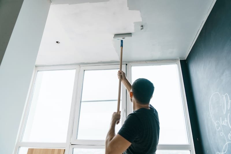 the man paints the walls and the ceiling in gray color, standing with his back to the camera. Focus on the roller. Painting and repair of the room.