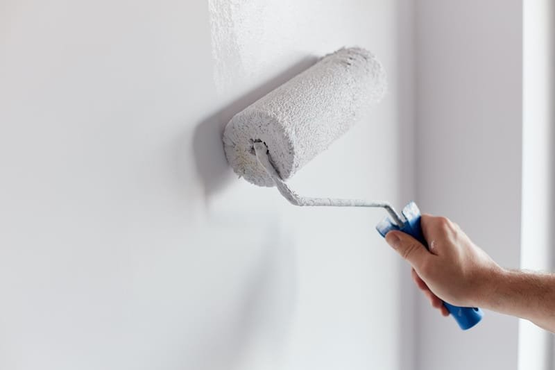 Male hand painting wall with paint roller. Painting apartment, renovating with white color paint