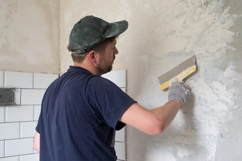 Caucasian man put plaster patching up the cracks on the wall. Renovation of flat.