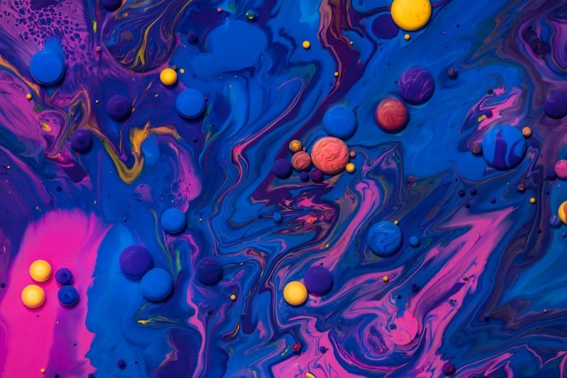 Acrylic paint balls abstract texture. Pink, blue and yellow liquids mix. Creative multicolor background. Bright colors fluid, flowing wallpaper design. Mixed pigments blue backdrop