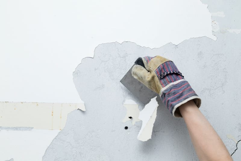 person scraping white paint of concrete wall during a home remodeling project
