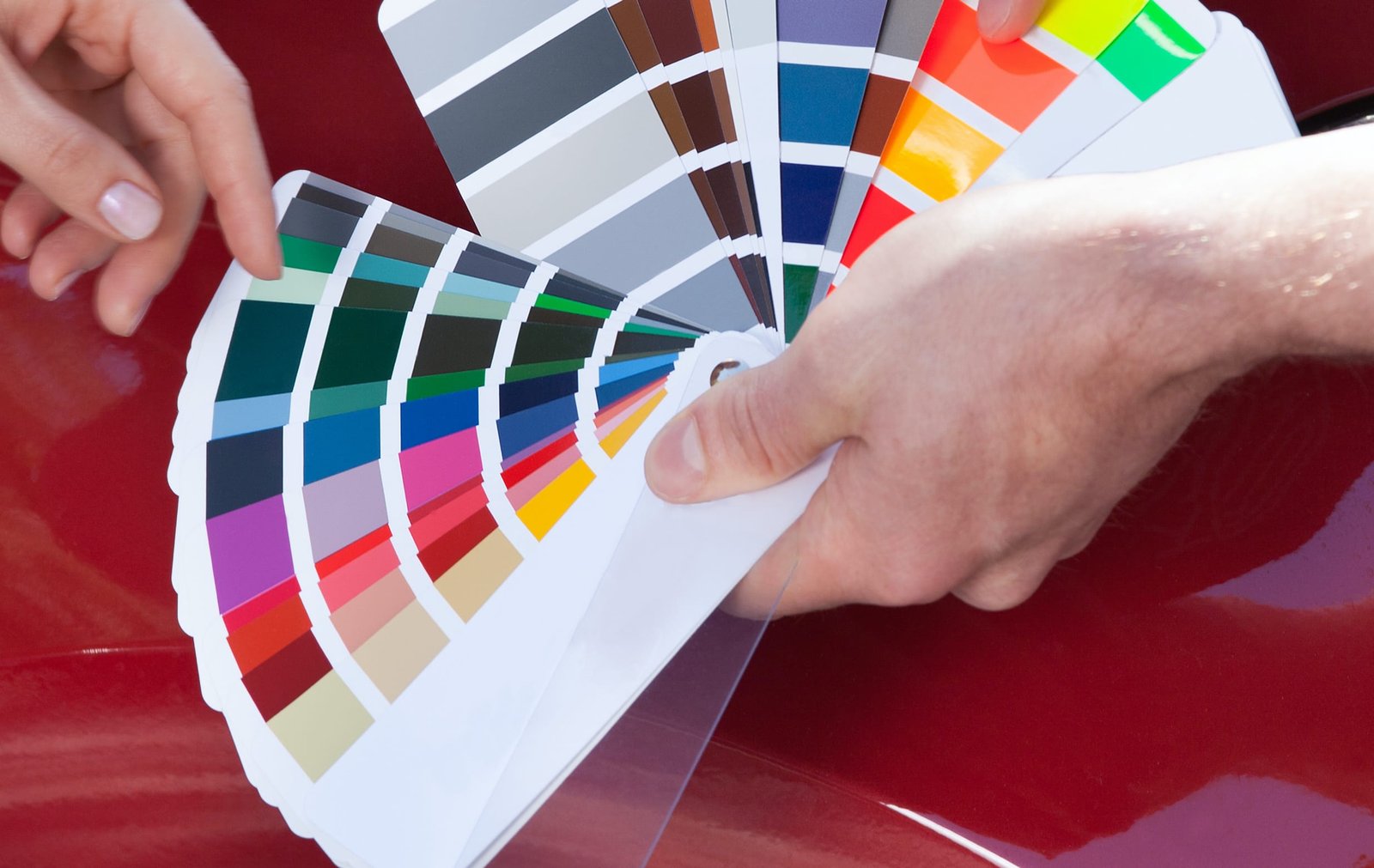 Cropped image of mechanic showing color samples to customer against car