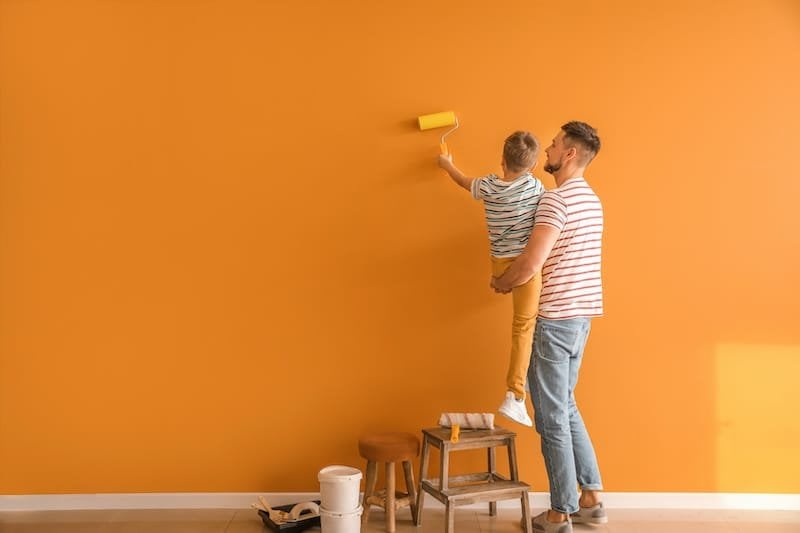 Little son helping his father to paint wall at home for paint prep