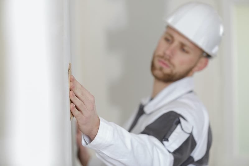 builder using sandpaper on interior wall