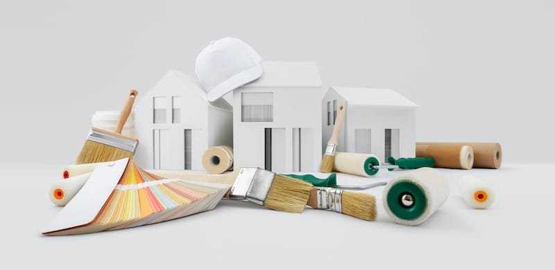 house painter tools, brushes, paint rollers, paper masking tape and colors swatches on desk with model house, supply and service in color shop in the hardware and store of building material.