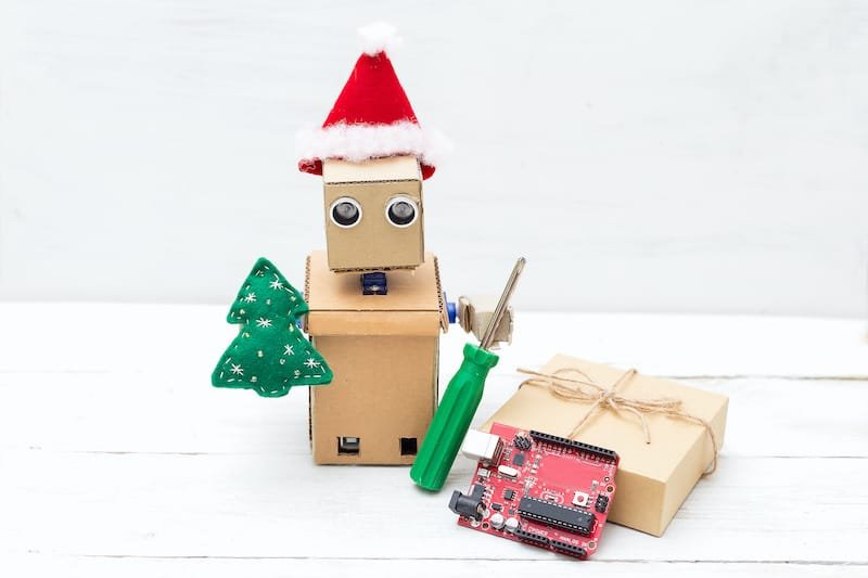 A robot in a santa hat holds a toy of christmas tree and screwdriver. Horizontal photo