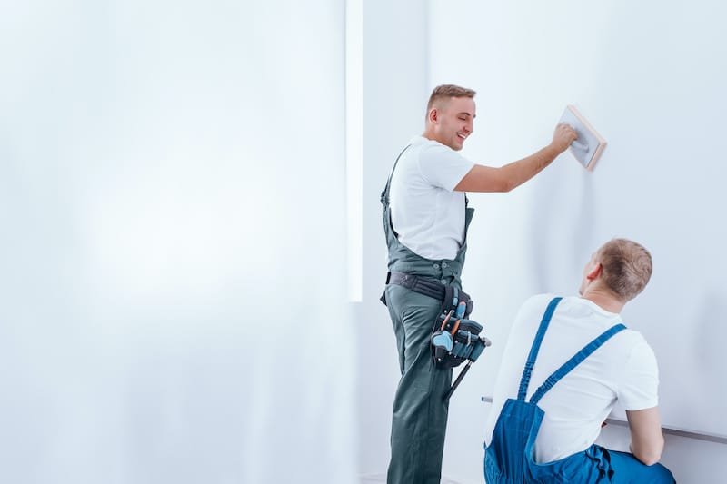 Home renovation crew preparing white wall for painting in the interior