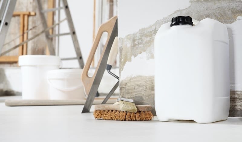 Indoor shot close up frontal view of bricklayer, plasterer or house painter tools on white floor with primer jerry can in home renovation site