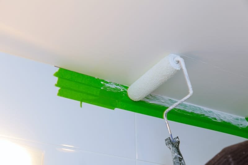 Rear view painter man painting the ceiling in bathroom, with paint roller