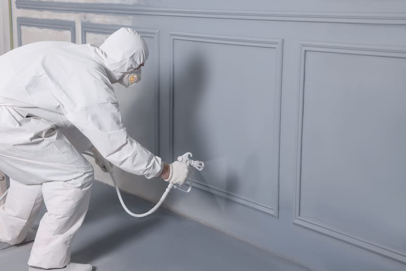 Decorator dyeing wall in grey color with spray paint indoors, space for text