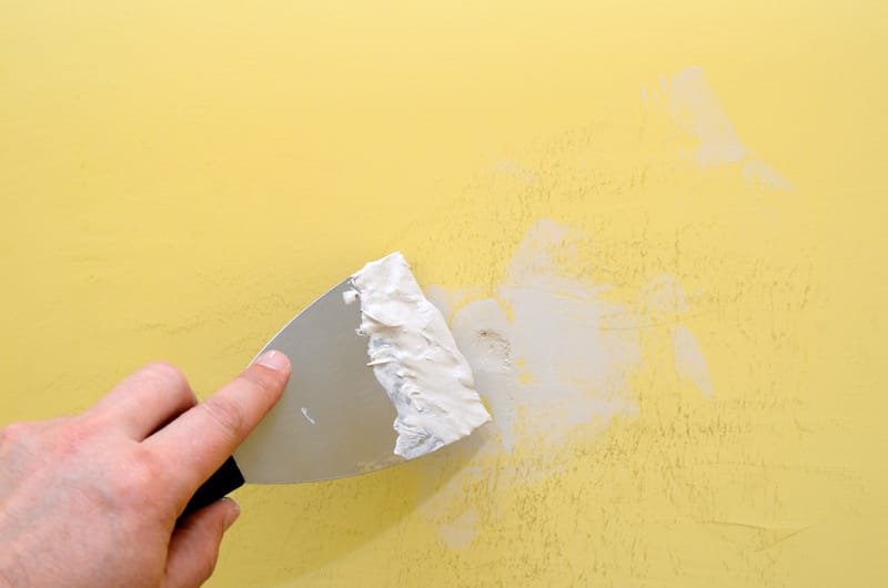 Hand with putty knife repair damaged wall